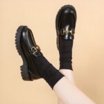 Photo d'une paire de mocassins à plateforme noire portée par une femme sur fond beige
