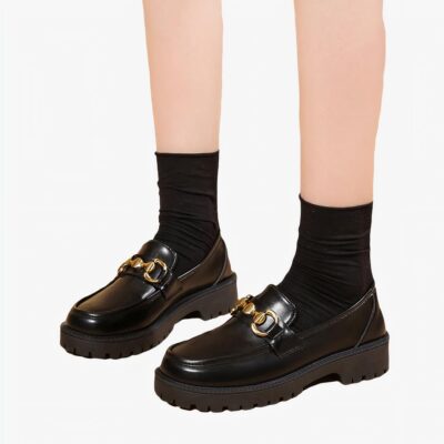 Photo d'une paire de mocassins à plateforme noire portée par une femme sur fond beige