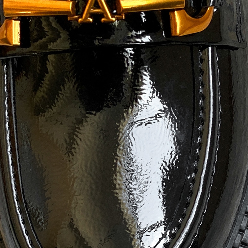 Photo d'un zoom sur un mocassin en cuir noir verni avec une chainette dorée et un A