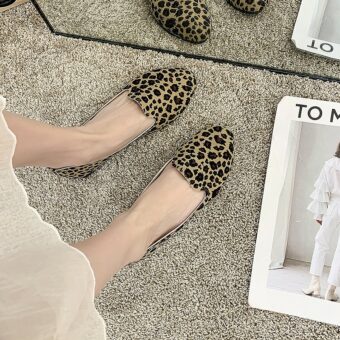 Paire de mocassins simple avec imprimé léopard vue du haut porté avec une jupe blanche et pieds nus. Le sol est en moquette beige et il y a un magazine blanc à côté