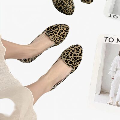 Paire de mocassins simple avec imprimé léopard vue du haut porté avec une jupe blanche et pieds nus. Le sol est en moquette beige et il y a un magazine blanc à côté