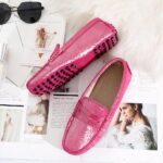 Photo d'une paire de mocassins roses posée sur des journaux, un plaid rose et près de lunettes de soleil