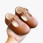 petit mocassin pour fille en faux cuir marron porter par une main d'adulte
