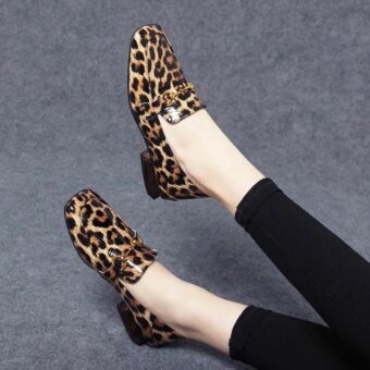 Sur fond gris, paire de jambes avec legging noirs et mocassins brillants avec talons carrés imprimé léopard