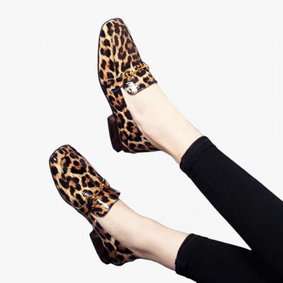 Sur fond gris, paire de jambes avec legging noirs et mocassins brillants avec talons carrés imprimé léopard