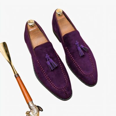 Mocassins violets en daim pour hommes, élégants, avec des pampilles sur le dessus et un embauchoir doré à côté.