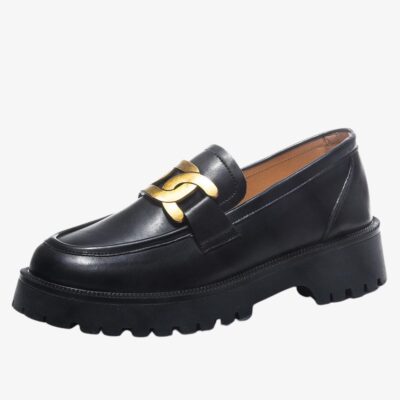Mocassin sophistiqué à plateforme pour femme de couleur noire avec une boucle dorée sur le dessus. Sur fond gris clair.