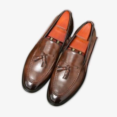 Des mocassins marrons en cuir à bout pointus et foncés avec des glands décoratifs