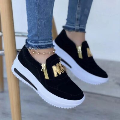 Paire de mocassins noirs portés par une femme avec un jean, dont on ne voit que les pieds