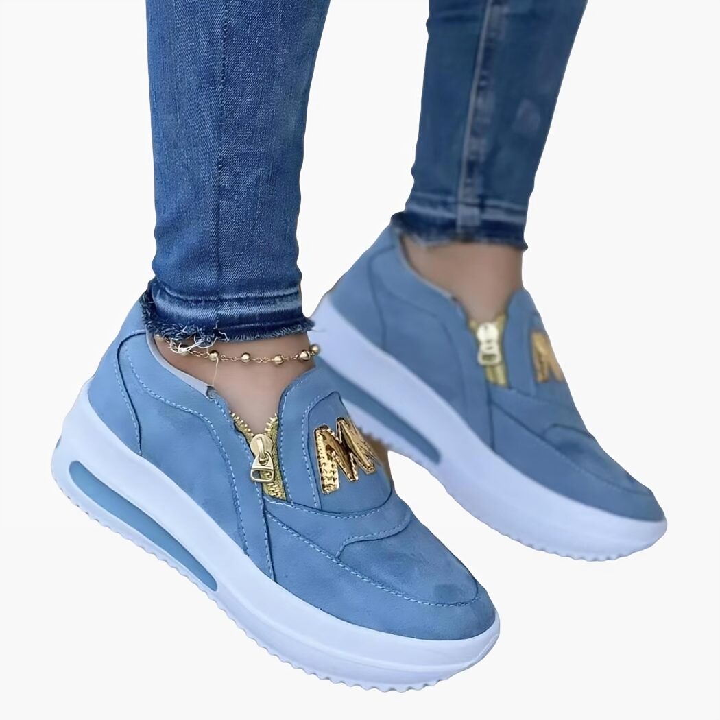 Mocassins bleus avec une fermeture dorée et portés par une personne dont on voit seulement les chevilles.