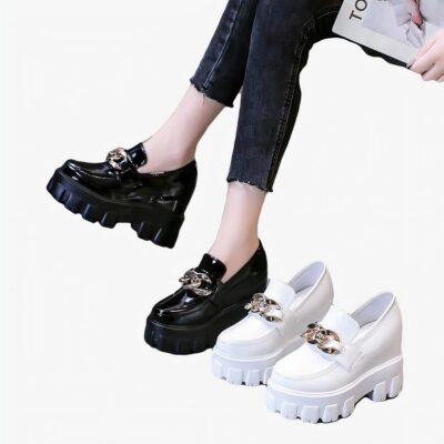 une paire de mocassins en cuir synthétique verni noir porté, une autre blanche posée à côté sur le sol, fond gris