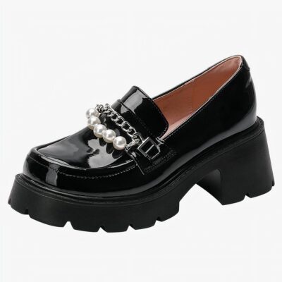 Un mocassin noir en cuir vernis à semelle épaisse noir et talon décoré d'une chaîne argentée et de perles blanches sur le dessus de la chaussure, l'intérieur est rose poudrée, sur un fond blanc uni.