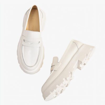 Une paire de mocassins en cuir lisse blanc simple avec semelle épaisse blanche posée sur un sol beige clair.