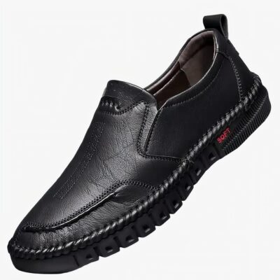 Mocassin noir posé sur un support blanc, fond gris.