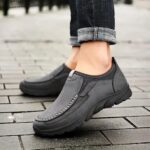 Mocassins gris tenu par une personne. On voit une rivière en fond.