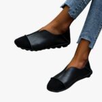 Paire de mocassins souples avec bout rond en suède noir et en cuir lisse avec coutures apparentes portée avec un jean sur un sol en carrelage gris clair