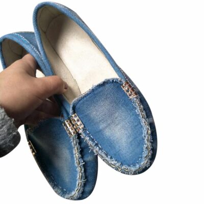 Paire de mocassins souples en denim bleu délavé avec semelle en caoutchouc beige avec picots portée pieds nus par une femme avec un jean déchiré bleu avec chevilles apparentes