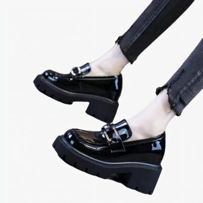 Des mocassins noirs vernis à talon et semelle épaisse noire aux pieds d'une femme se tenant debout et portant un jean noir slim.