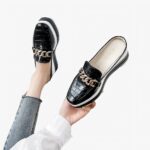 Femme près d'un canapé blanc tenant un mocassin à la main et portant au pied gauche un mocassin noir