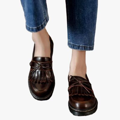 on voit les pieds d'une femme en jean qui porte des mocassins marrons à talons carrés avec une frange dans le style vintage
