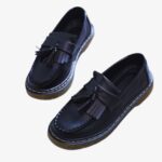 on voit sur un fond blanc une paire de mocassins à glands et à franges en cuir synthétique pour femme, ils sont noirs