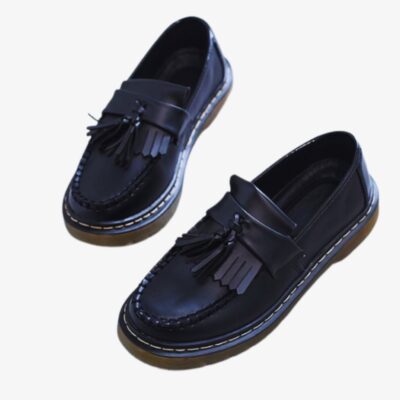 on voit sur un fond blanc une paire de mocassins à glands et à franges en cuir synthétique pour femme, ils sont noirs