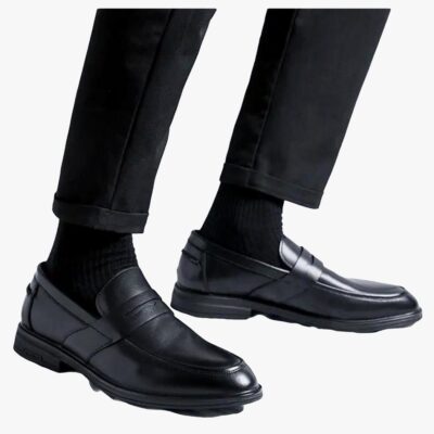 on voit sur un fond clair le bas des jambes d'un homme il porte un pantalon noir et des mocassins noirs classiques en cuir synthétique pour homme