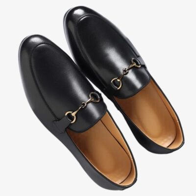 Mocassin noir à boucle dorée à enfiler et en cuir végan sur fond blanc cassé.