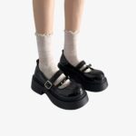 Jambes de femme avec des mocassins noirs à plateforme avec deux brides, portant des chaussettes hautes blanches.