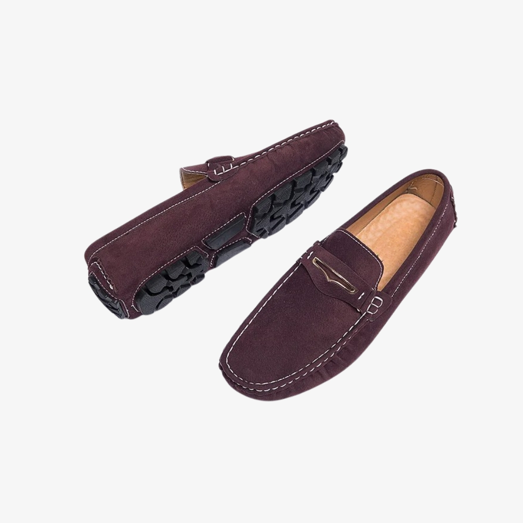 Mocassins confortables pour homme en daim de couleur bordeaux. Ces chaussures élégantes présentent des coutures contrastées blanches, une boucle métallique discrète sur le dessus et une semelle crantée noire pour une meilleure adhérence. L'intérieur matelassé assure un confort optimal au quotidien.