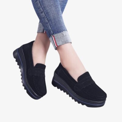 Mocassins pour femme en daim noir, élégants et confortables, dotés de semelles compensées crantées pour une meilleure stabilité. Leur design inclut des détails décoratifs sur le dessus et une couture apparente, parfaits pour un style moderne et décontracté.